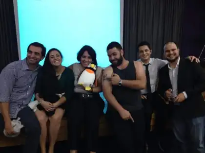 Seis pessoas sorrindo com um pinguim de pelúcia